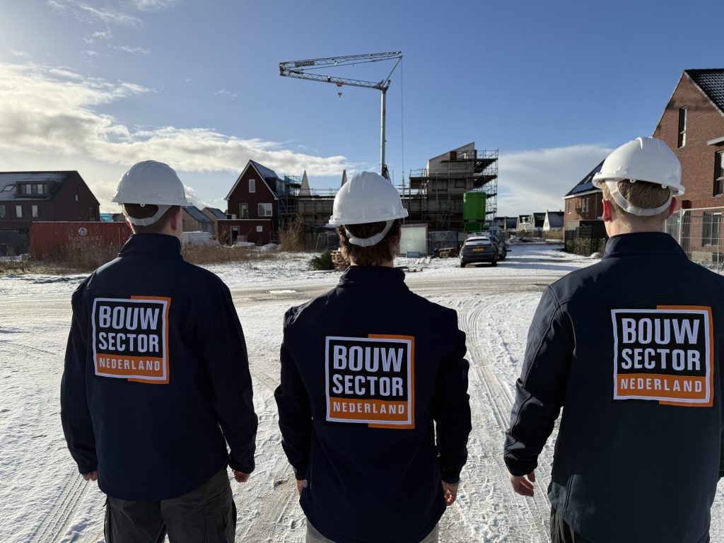 Vakmensen van Bouwsector Nederland in werkkleding kijken uit over een rij nieuwe woningen