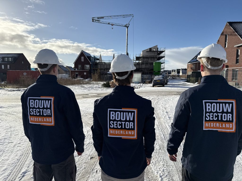 Drie vakmensen van Bouwsector Nederland met witte helm voor een rij nieuwe woningen